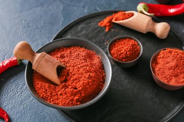 Koyu arkaplanda kırmızı biber tozu olan kâseler ve kepçeler