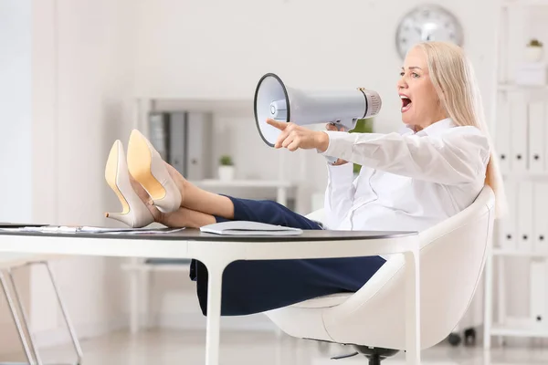 Stressed mature woman with megaphone in office