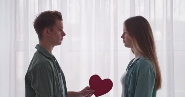 Feliz Casal Adolescente Com Papel Vermelho Coração Abraçando Perto Janela — Vídeo de Stock