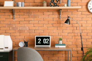Ofiste tuğla duvarın yanında dizüstü bilgisayarı olan şık bir iş yeri.