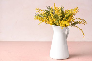 Hafif arka planda güzel mimoza çiçekleri olan sürahi.