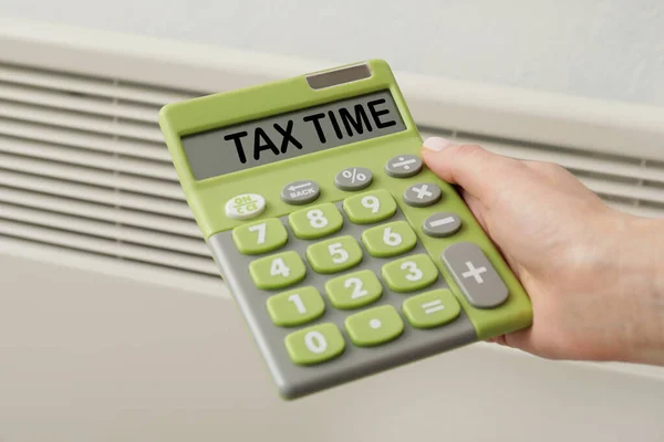 Woman with calculator near radiator, closeup. Concept of tax deadline