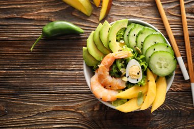 Tahta arka planda mango, karides ve sebzeli bir kase taze salata.