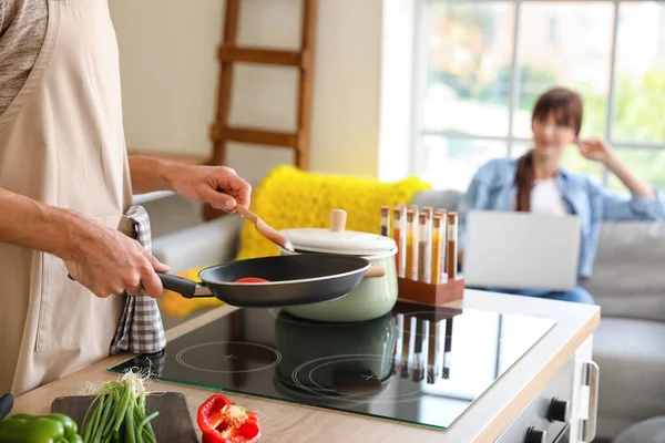 Young Man Cooking Dinner While His Wife Using Laptop Kitchen — Stock Photo, Image