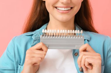 Pembe arka planda diş rengi çizelgesi olan genç bir kadın. Yakın plan.