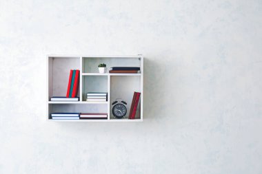 Rafta kitaplar ve çalar saat asılı.