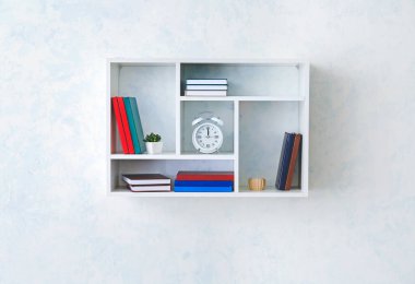 Rafta kitaplar ve çalar saat asılı.