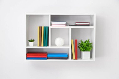 Rafta kitaplar ve bitkiler asılı.