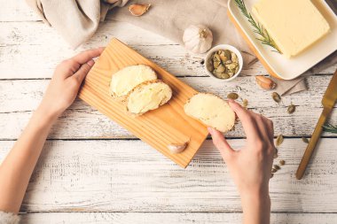 Elinde taze ekmek dilimleri ve hafif ahşap arka planda tereyağı tutan bir kadın.
