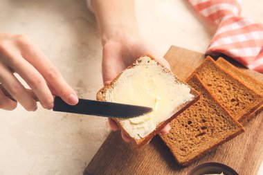Kadın arka planda taze ekmek dilimine tereyağı sürüyor, yakın plan.