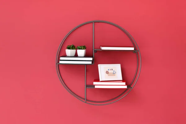 Shelf with books, picture and plants hanging on color wall