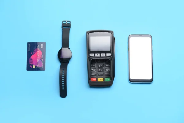 Payment terminal with credit card, mobile phone and smart watch on color background