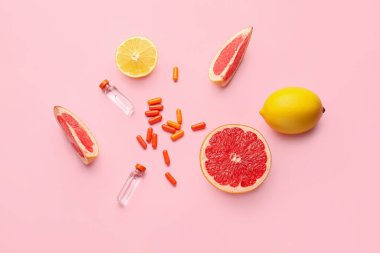 C vitamini şişeleri, haplar ve renkli arkaplanda turunç meyveleri