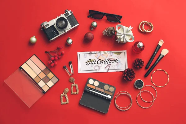 Gift certificate, decorative cosmetics and female accessories on color background