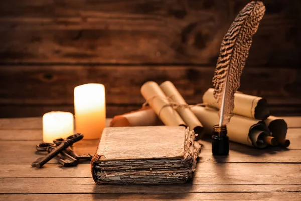 Old book with scrolls, feather, keys and candles on wooden background