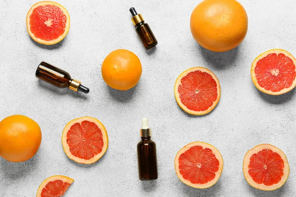 Bottles of essential oil and grapefruits on light background