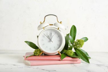 Alarm saati, defterler ve arka planda yeşil dallar