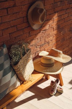 Odadaki tuğla duvarın yanında kadın kamış çantalı ve şapkalı bank.