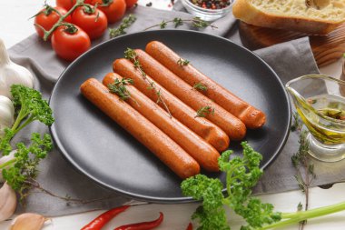 Hafif ahşap arka planda lezzetli sosisler, sebzeler ve otlarla kaplı tabaklar, yakın plan.