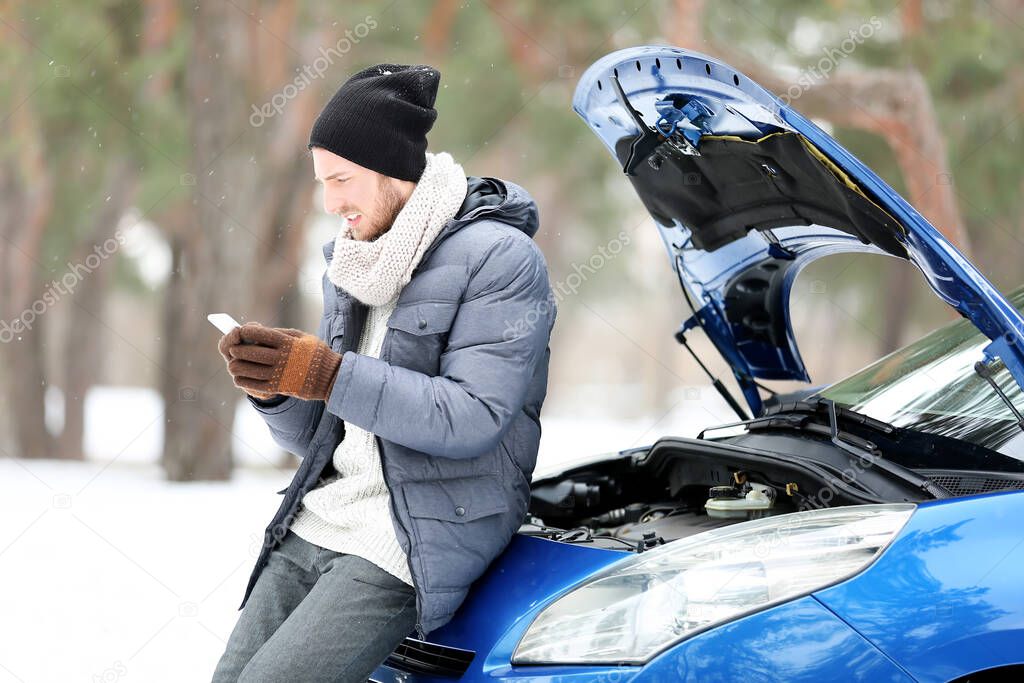 Stressed young man with mobile phone near broken car outdoors