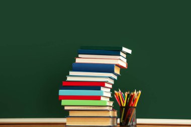 Renk arkaplanında kalemler olan kitap yığını ve tutucu