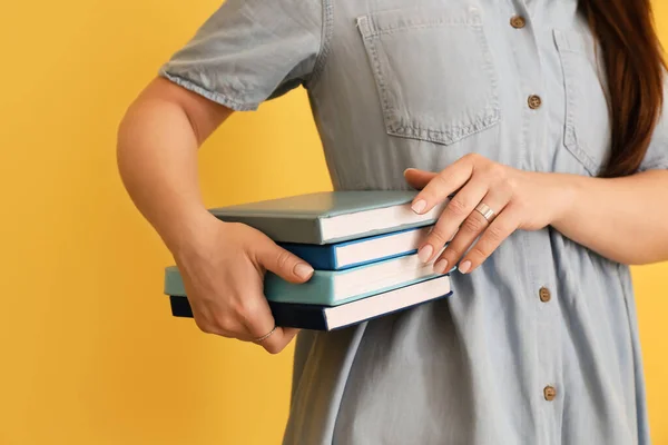 色の背景に本のスタックを持つ女性 — ストック写真