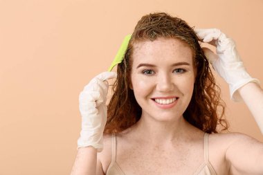 Arka planda kına saç boyası kullanan genç bir kadın.