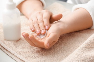 Genç bir kadın hafif arka planda ellerine krem sürüyor.