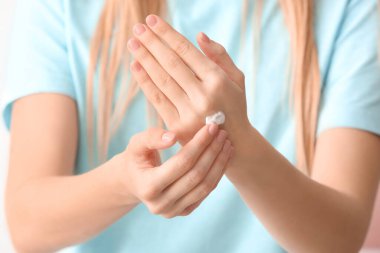 Genç bir kadın ellerine krem sürüyor, yakın plan.