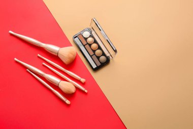 Renk arkaplanında şık makyaj fırçaları ve göz falı paleti