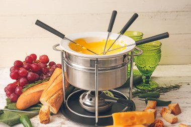 Peynirli fondü ve beyaz ahşap arka planda farklı atıştırmalıklar.