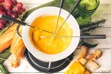 Peynirli fondü ve beyaz ahşap arka planda farklı atıştırmalıklar.