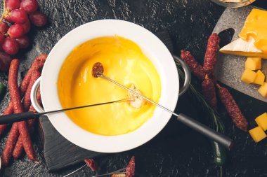 Koyu arkaplanda peynir fondüsüne batırılmış kızarmış ekmek çubukları.