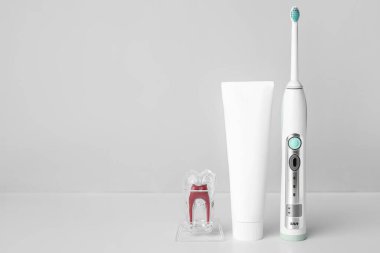 Yapıştırıcılı elektrikli diş fırçası ve arka planda plastik diş modeli.