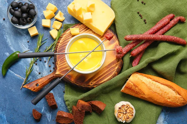 Cheese fondue and different snacks on color background