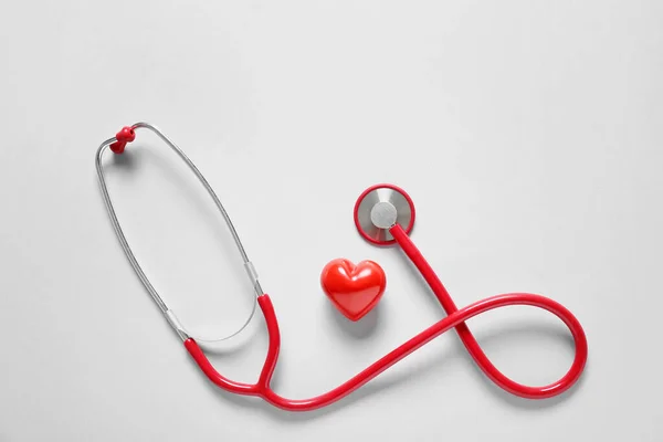 Modern stethoscope and heart on light background