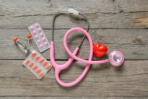 Modern stethoscope, medicines and heart on wooden background