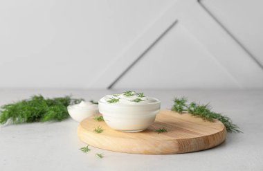 Bir kase lezzetli ekşi krema ve gri arka planda bitkiler.