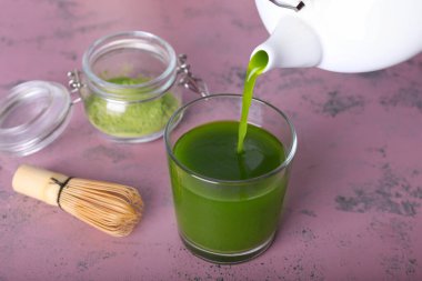 Çaydanlıktan bardağa renkli arkaplan üzerine kibrit çayı dökülüyor