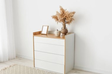 Çekmecelerin modern sandığı, odanın ışık duvarının yanında.