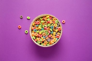 Renkli arkaplanda lezzetli mısır gevreği halkaları olan bir kase