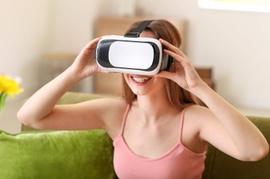 Evde sanal gerçeklik gözlüklü genç bir kadın var.