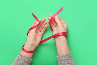 Female hands with red ribbon on color background