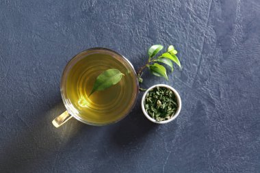 Cup of green tea and dry leaves on dark background