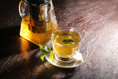 Teapot and cup of hot beverage on dark background