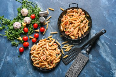 Frying pan and plate with tasty cajun chicken pasta on color background