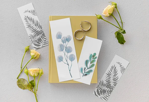 Book with bookmarks and flowers on light background