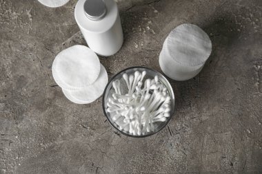 Koyu arkaplanda pamuklu çubuk, ped ve bir şişe kozmetik ürünü olan cam.