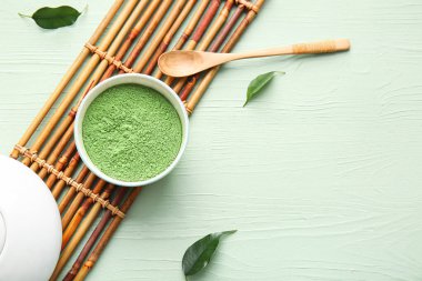 Renkli ahşap zemin üzerine pudralanmış kibrit çayı, kaşık ve bambu hasırı.