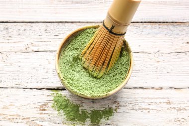 Pudralanmış kibrit çayı ile kase ve hafif ahşap arka planda chasen.